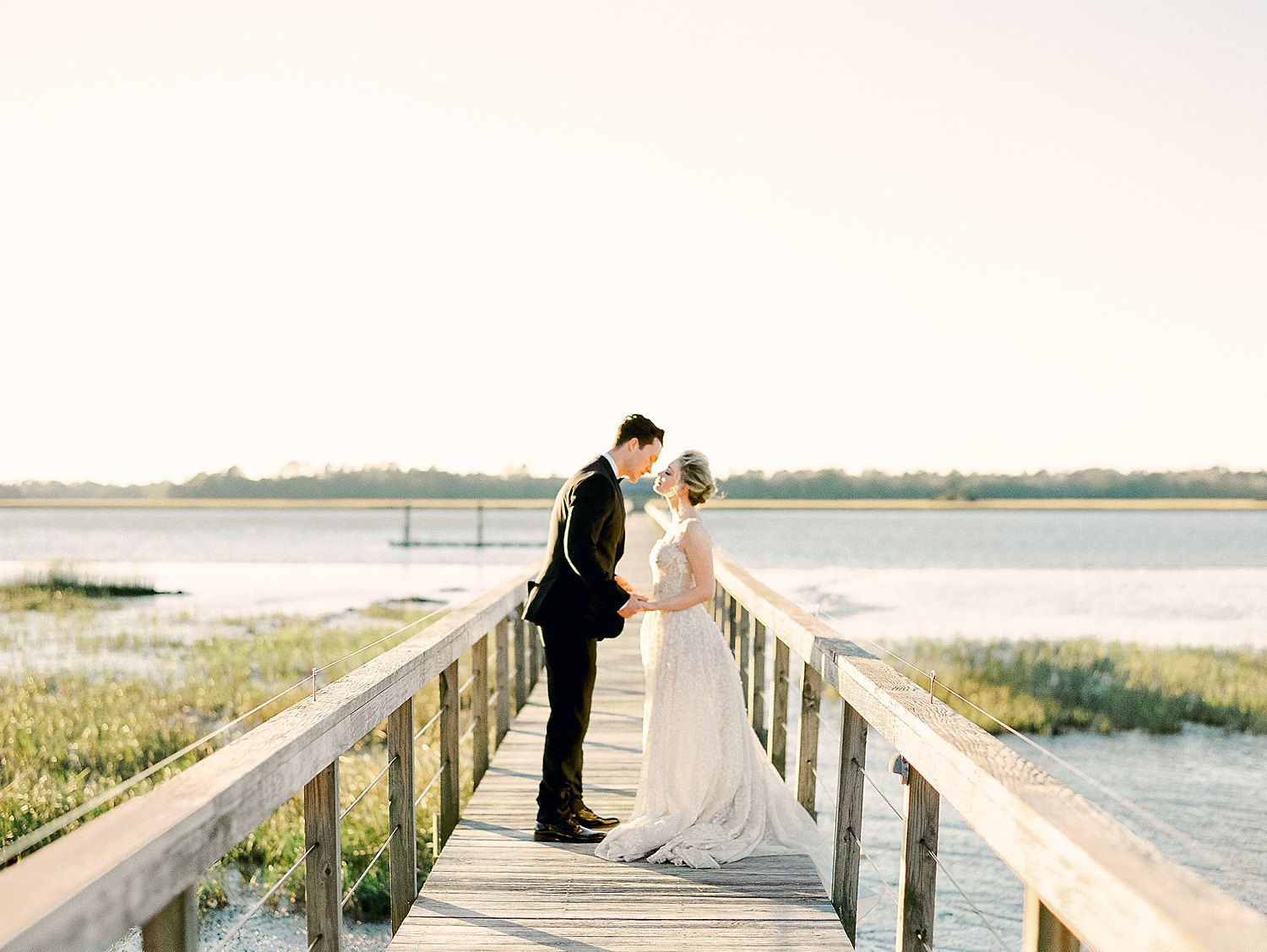 Bride and groom holding hands and kissing on wooden dock on river at Charleston Wedding