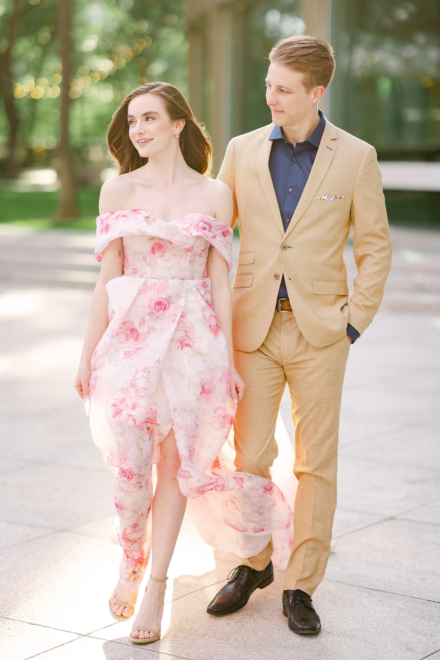 smiling woman in Pink floral gown walking with man in tan suite and blue shirt