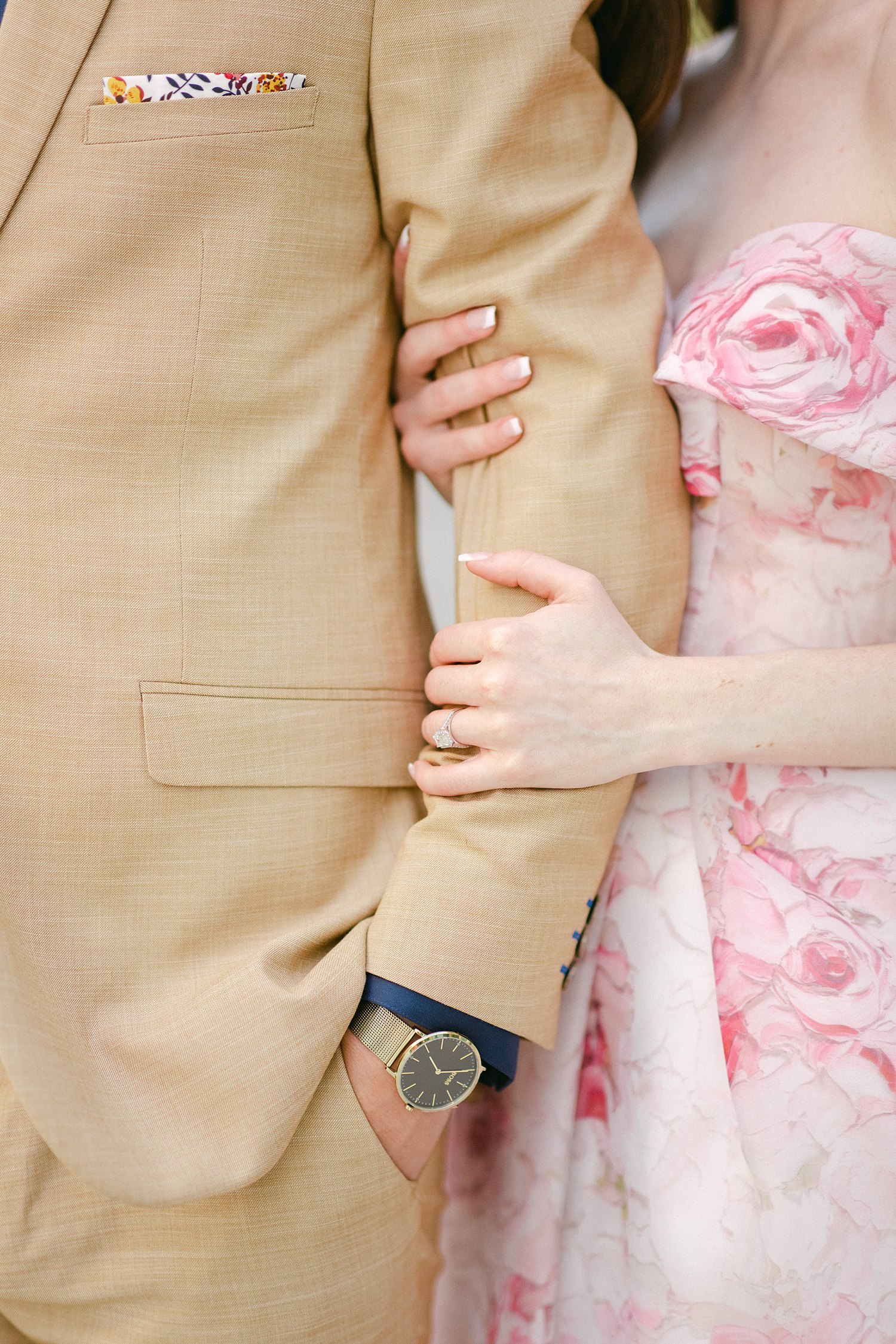 Woman in Pink floral gown hand and arm around man in tan suite