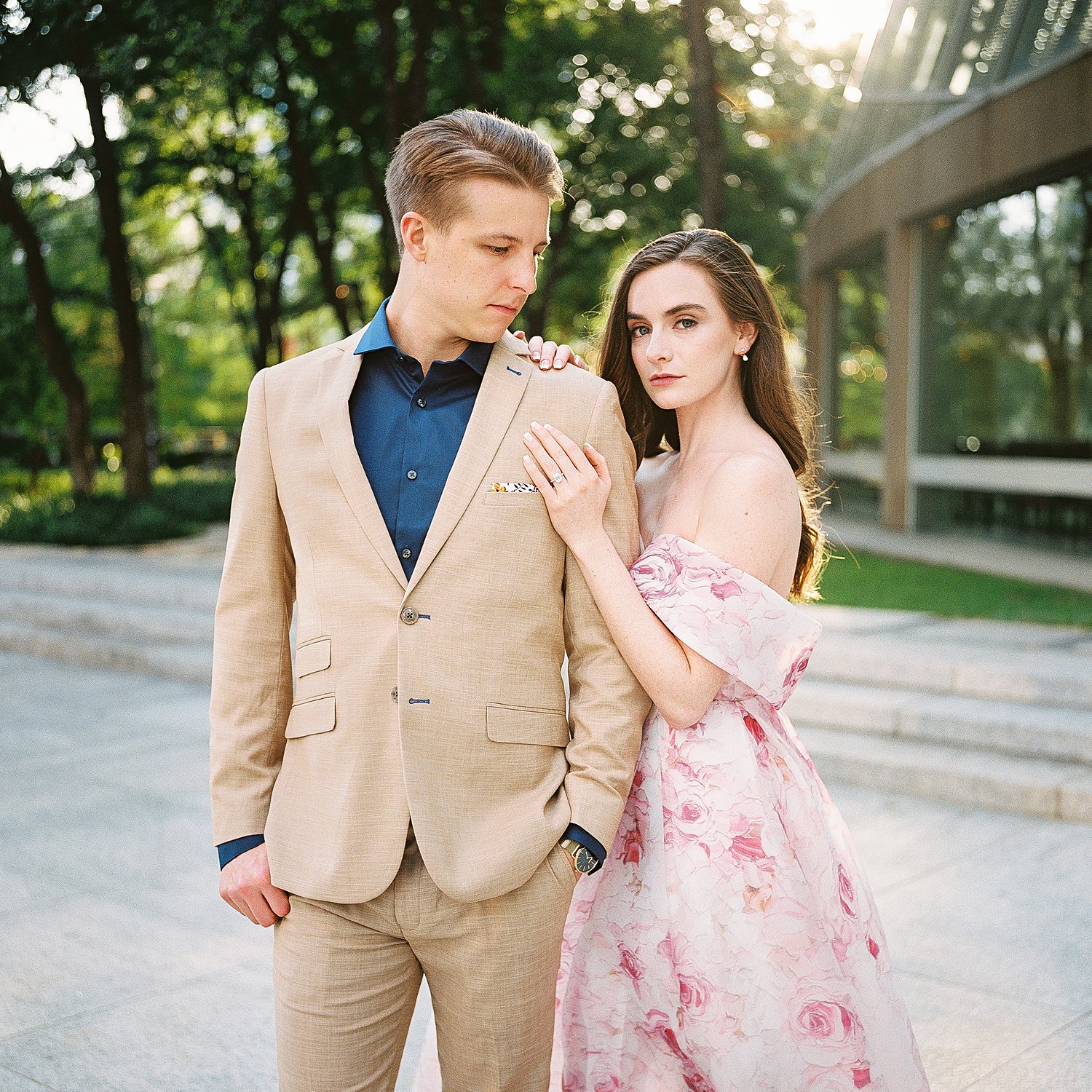 Woman in Pink floral gown arm around man in tan suite and blue shirt with gold watch