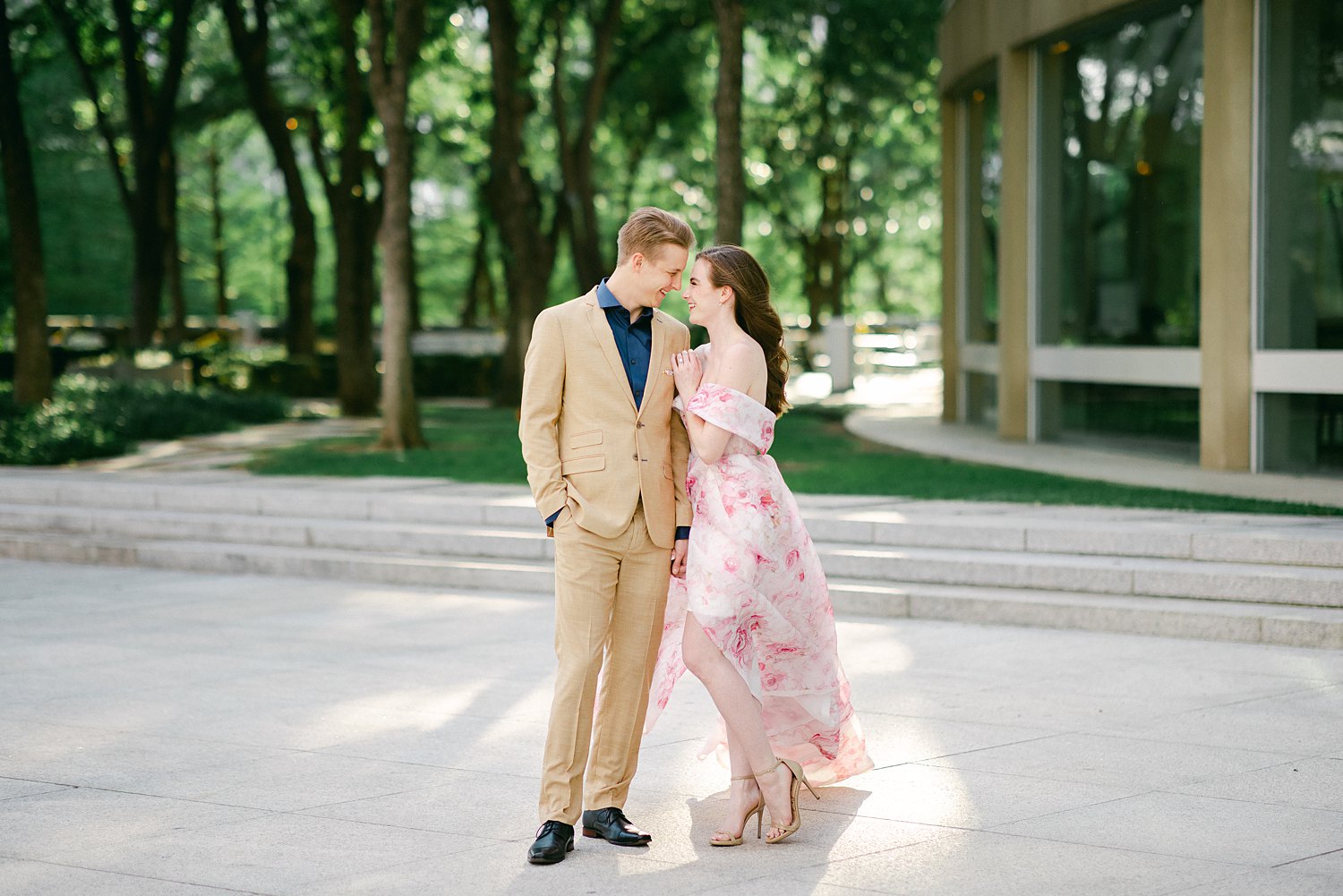 Laughing woman in Pink floral gown arm around man in tan suite and blue shirt