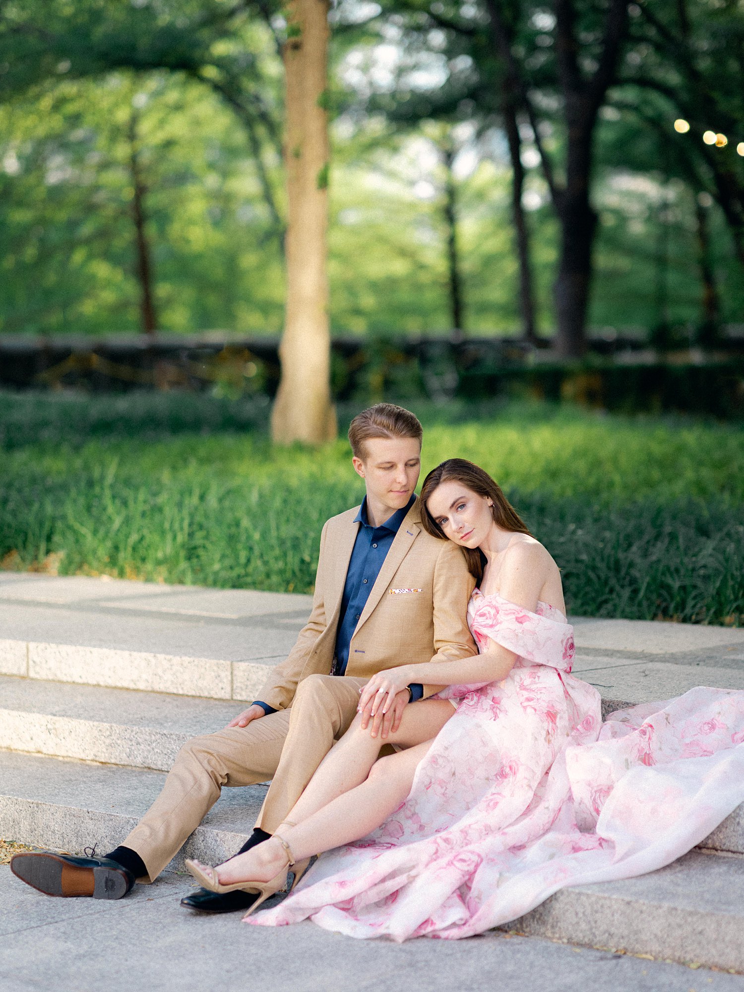 smiling woman in Pink floral gown sitting with man in tan suite and blue shirt dallas garden engagement