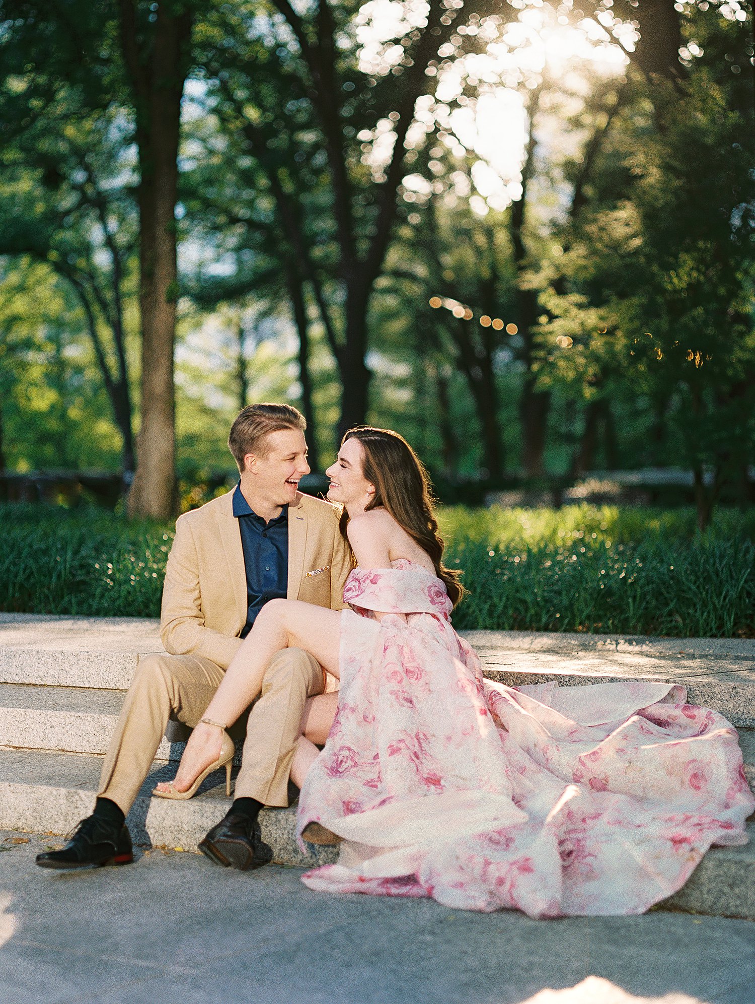 laughing woman in Pink floral gown sitting with man in tan suite and blue shirt dallas garden engagement