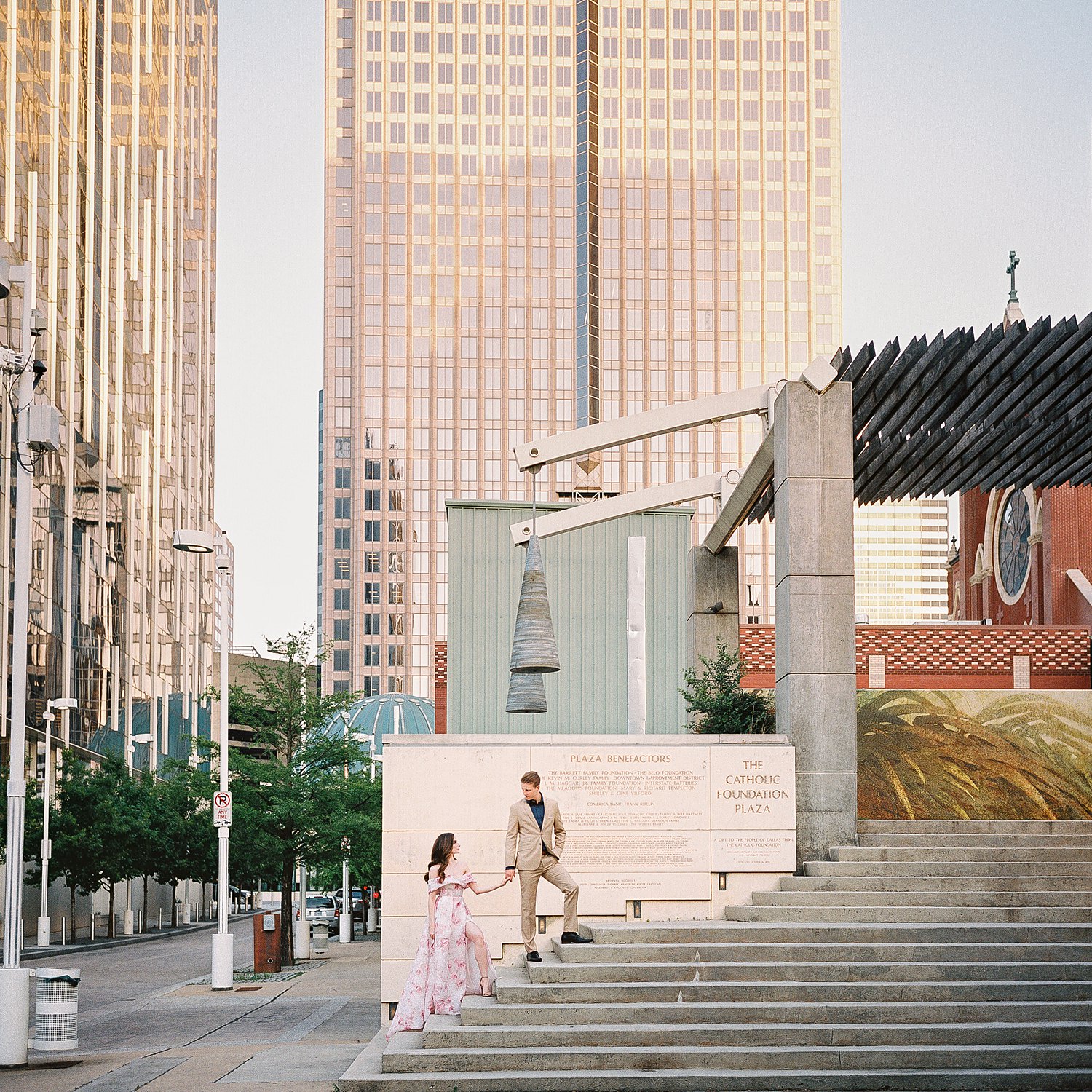 woman in Pink floral gown walking up stairs with man in tan suit at downtown Dallas arts district