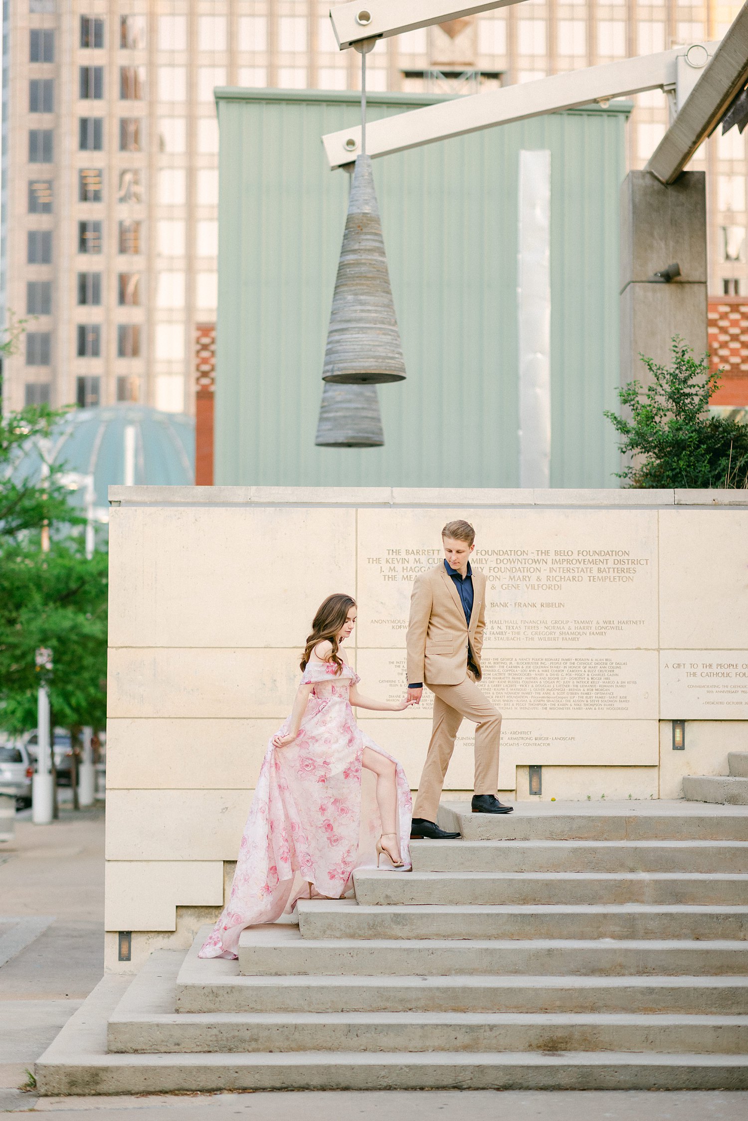 woman in Pink floral gown walking up stairs with man in tan suit at downtown Dallas