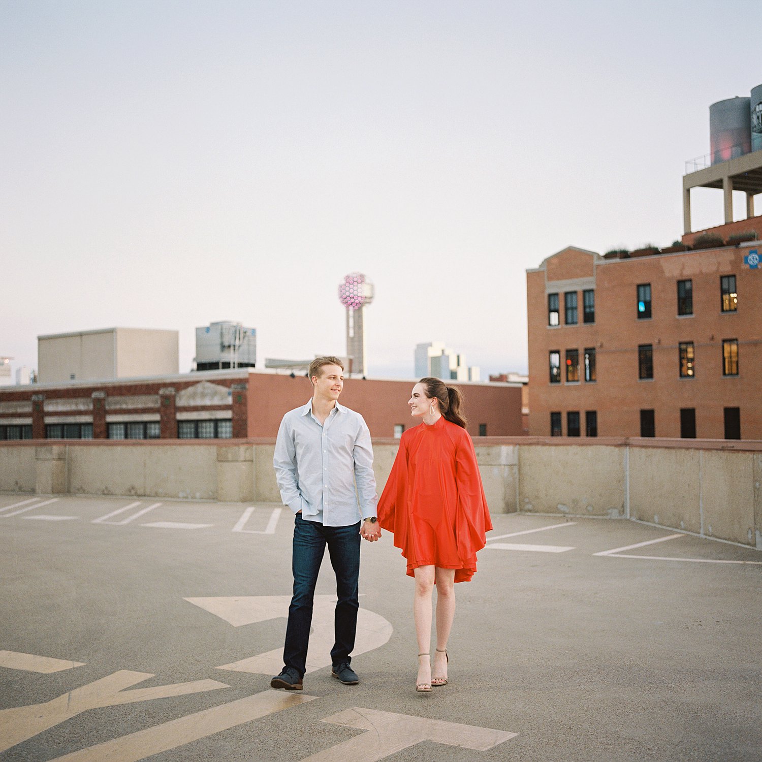 woman in orange dress and pony tail walking with man downtown Dallas engagement session