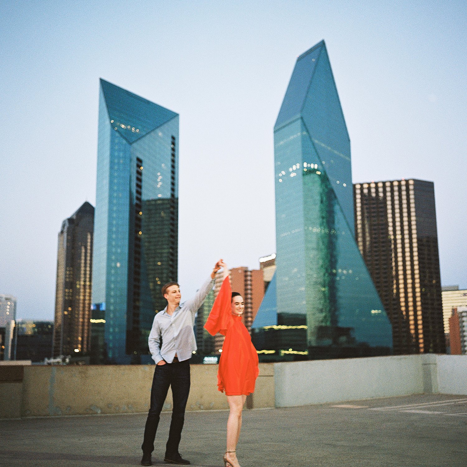 woman in orange dress and pony tail twirling with man on downtown Dallas rooftop