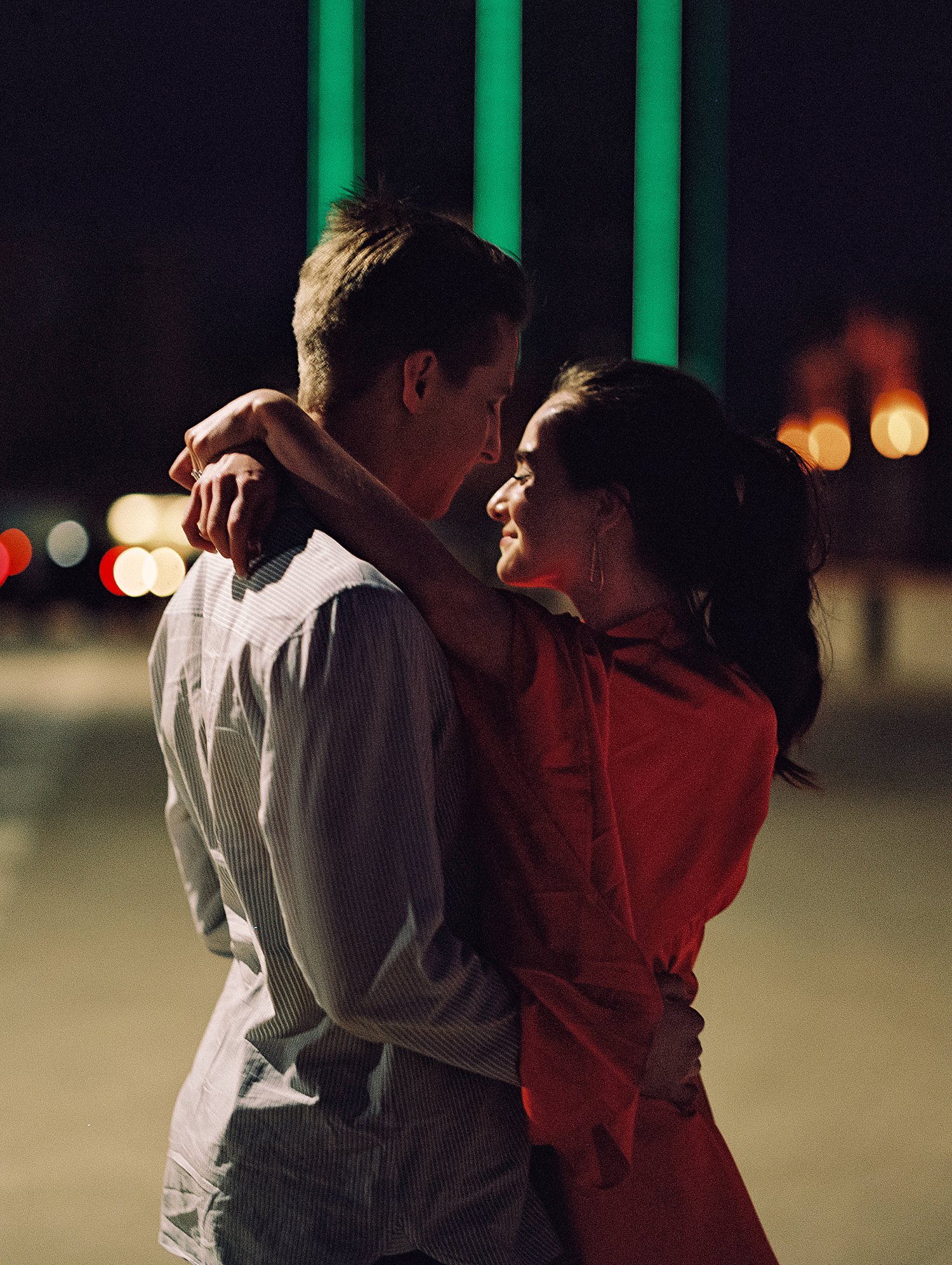 woman in dress and pony tail hugging man downtown Dallas engagement session at night
