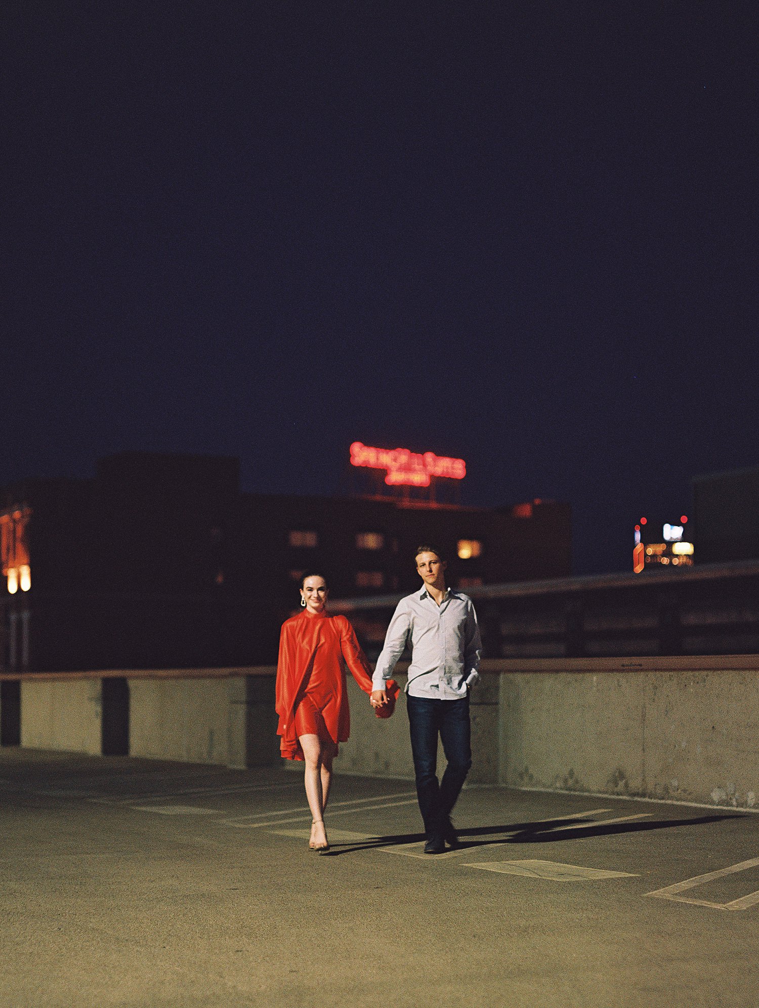 woman in orange dress and pony tail walking with man downtown Dallas engagement session at night