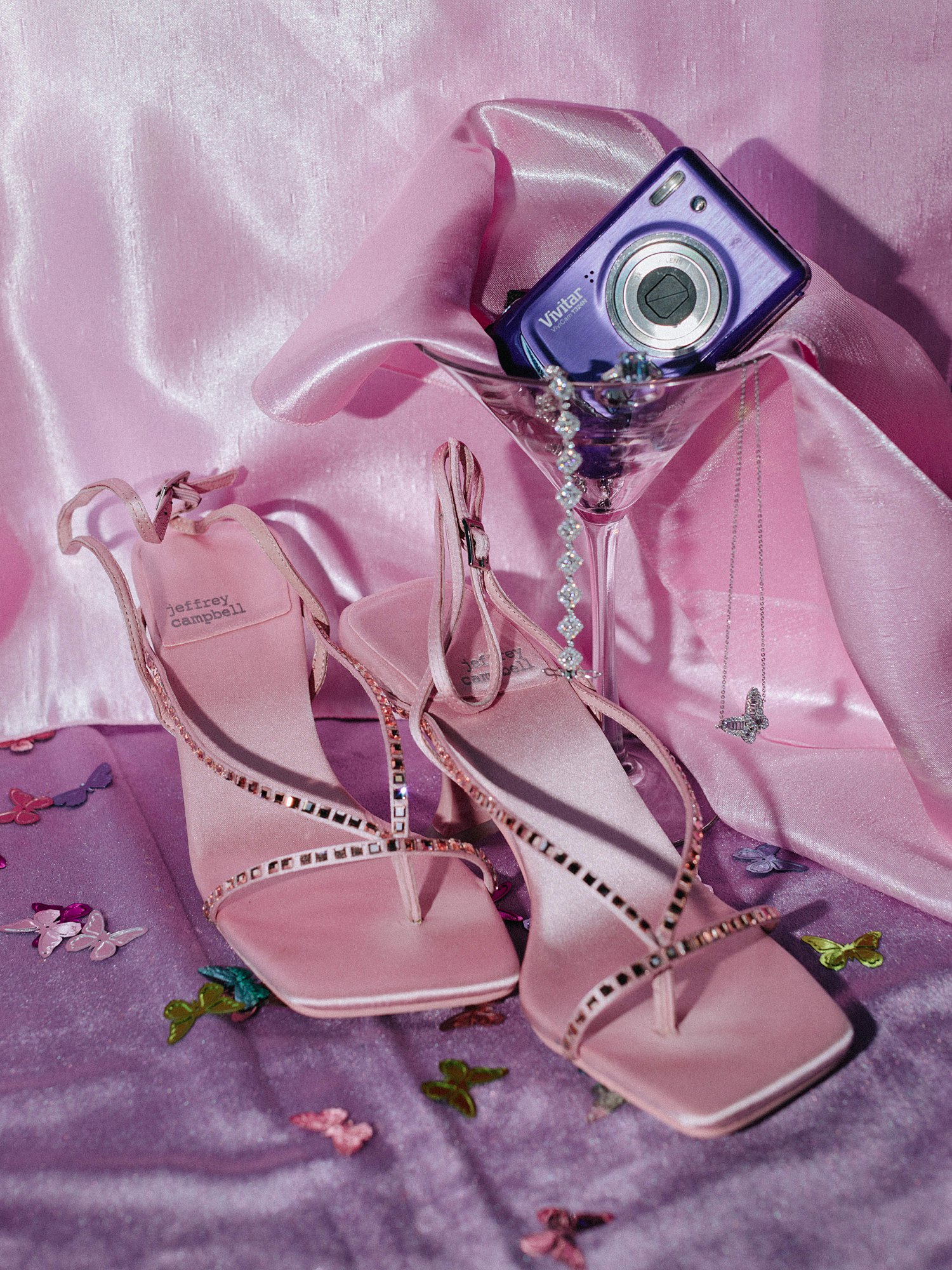 Digicam camera in martini glass next to pink heels and diamond bracelet, 2000's inspired wedding 