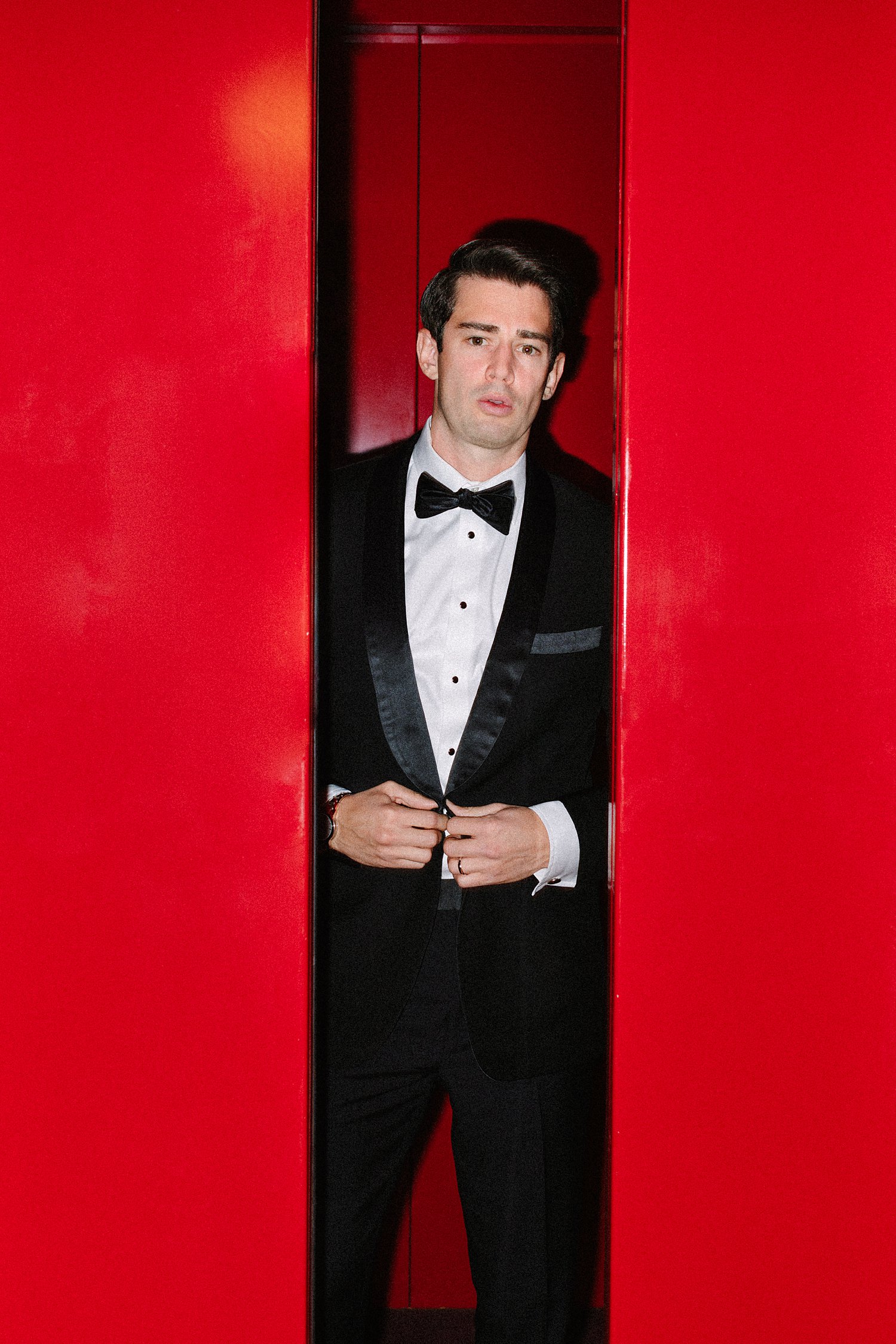 Man in black tuxedo and bowtie standing in red elevator at Virgin Hotel Dallas