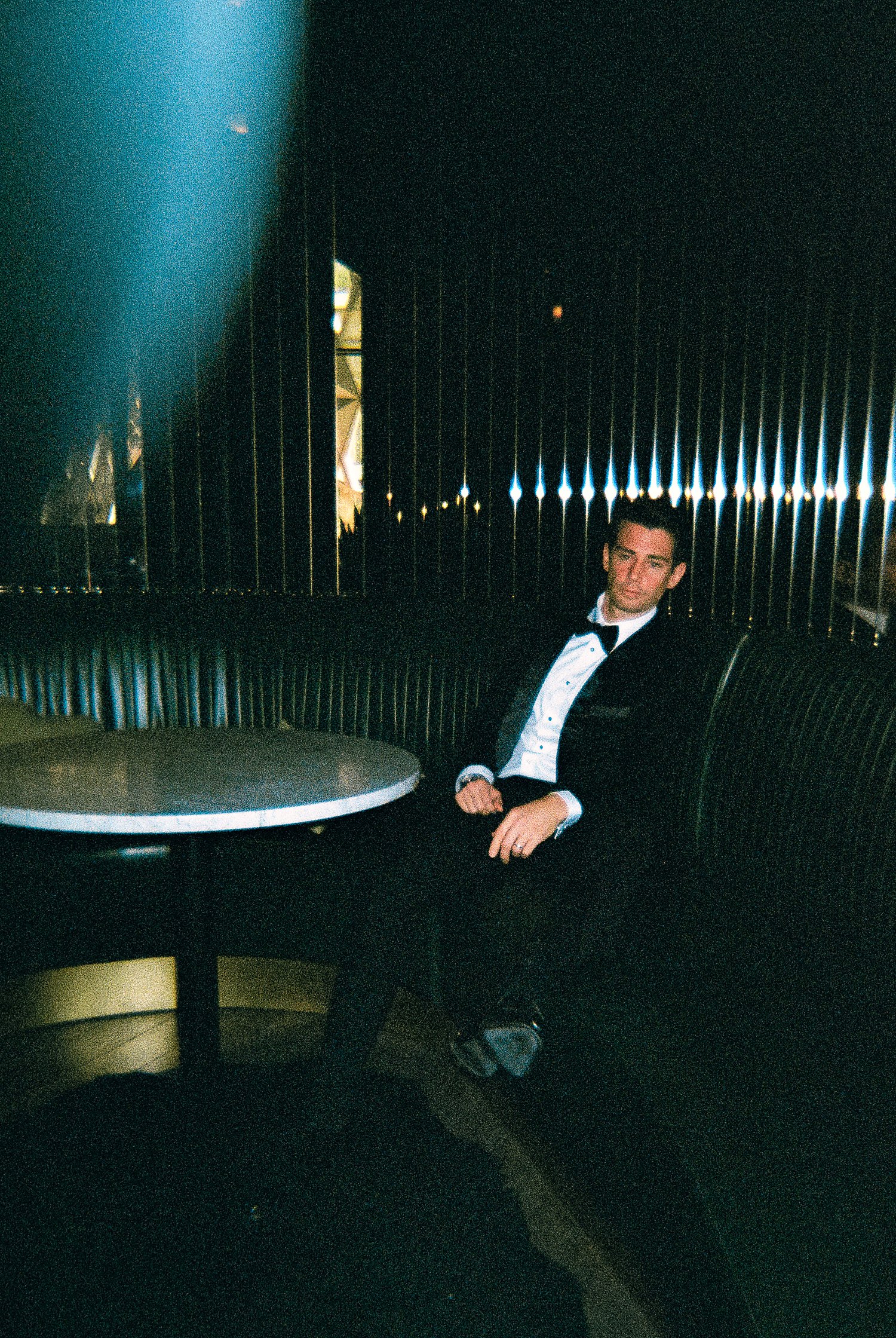 35mm Film, Groom in black tuxedo sitting in green booth at Virgin Hotel Dallas