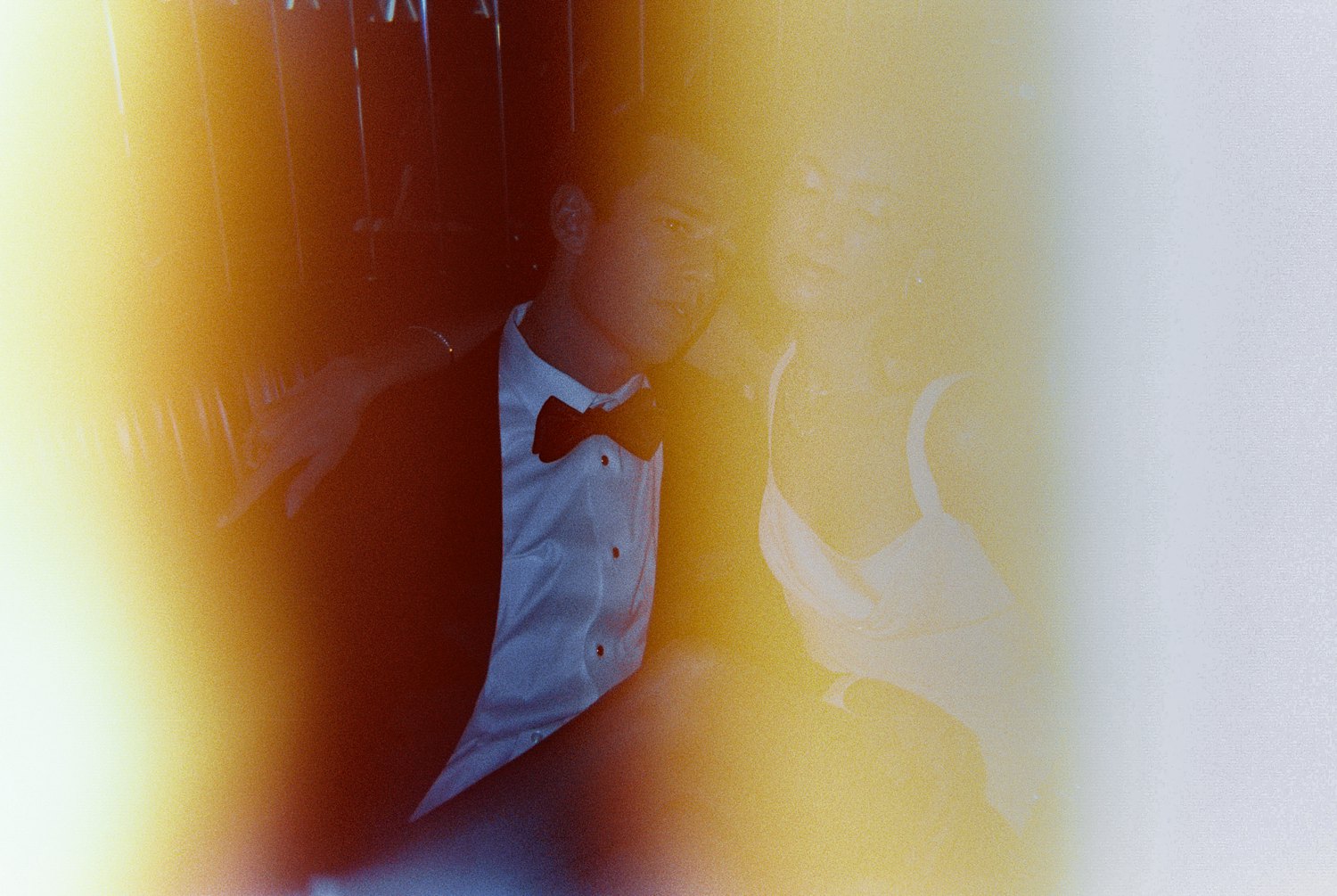 man in black tuxedo and bowtie with woman in white dress light leak film print