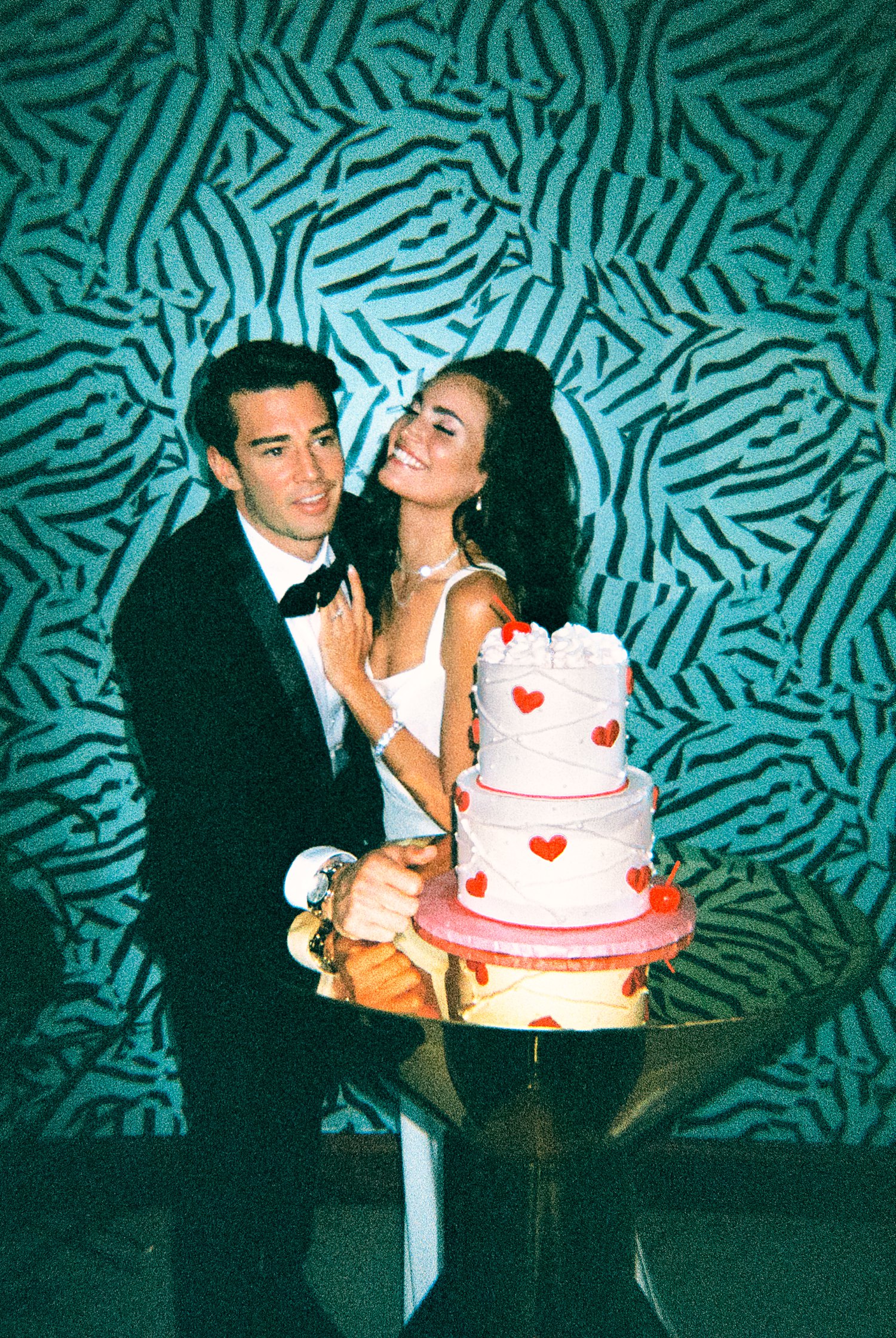 Grainy Film Photo of bride and groom smiling by red heart white cake and blue wallpaper at Virgin Hotel Dallas