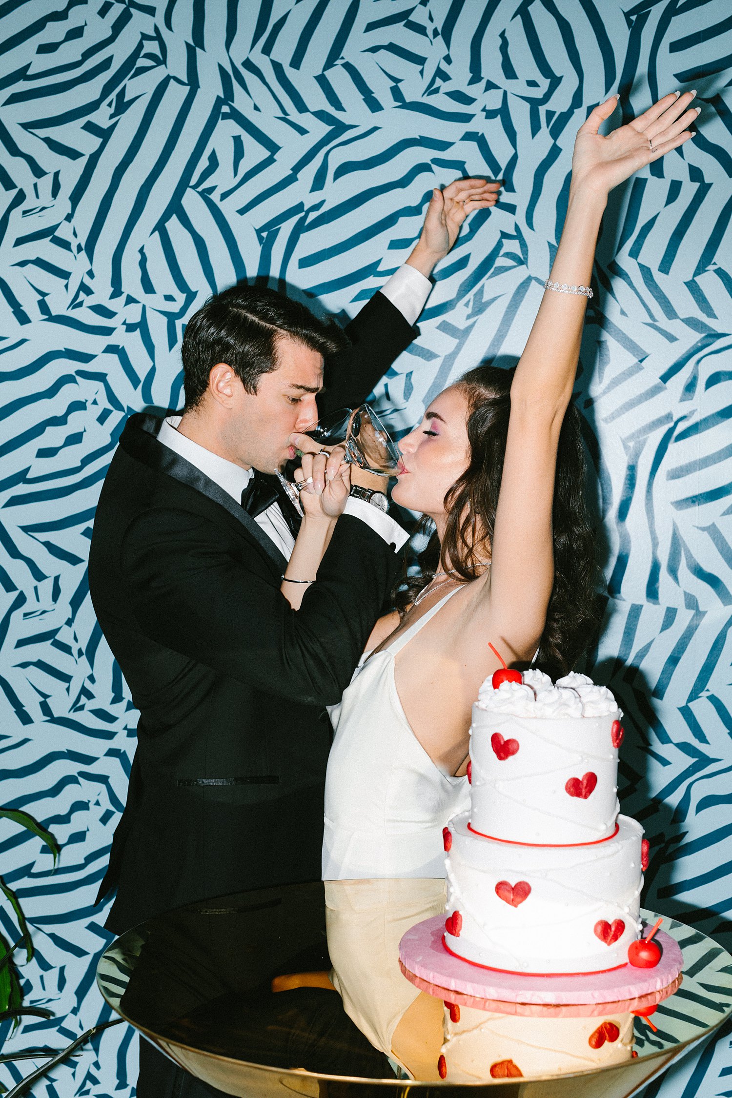 bride and groom toasting behind red heart white cake and blue wallpaper
