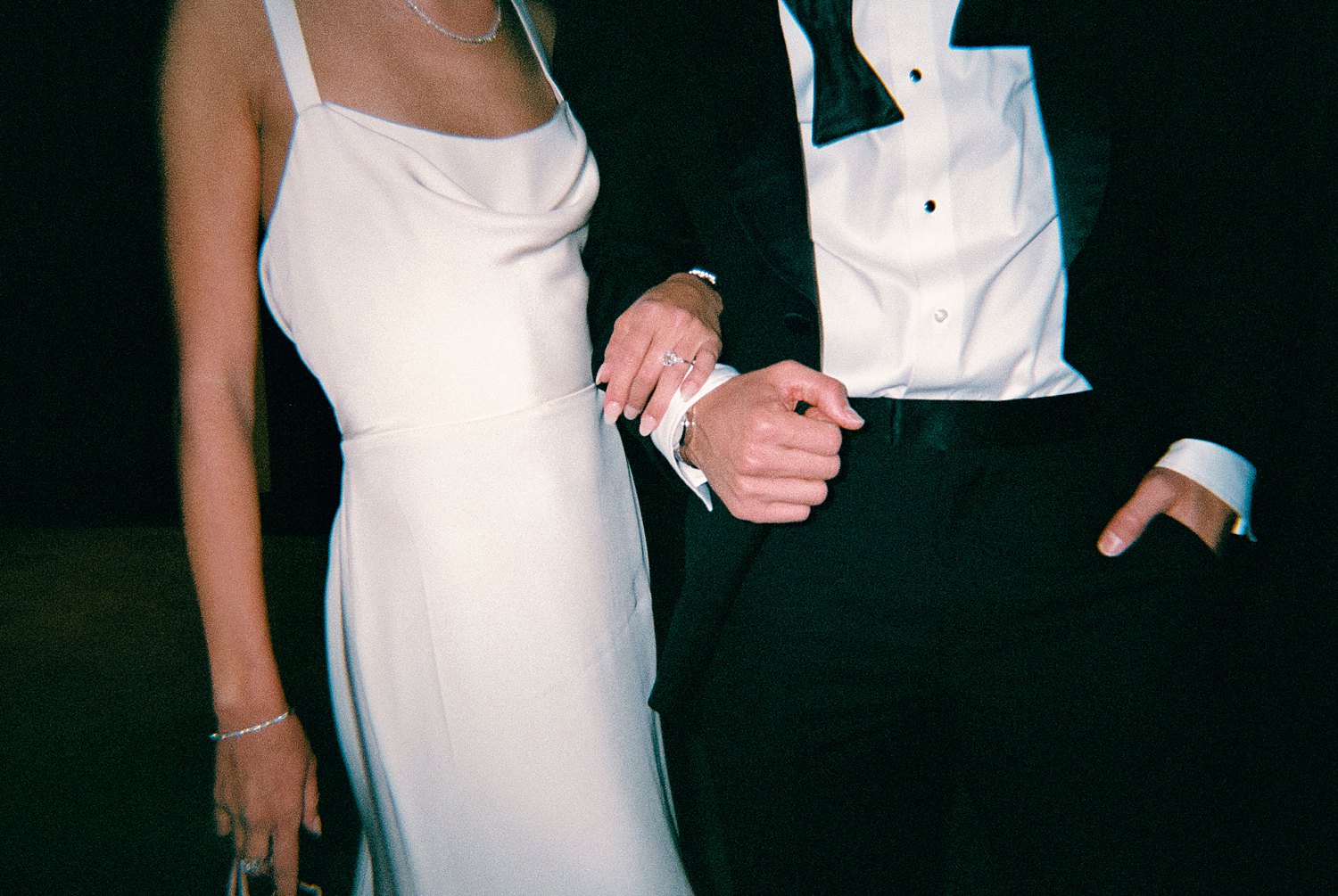 Man in black tuxedo clasping arms with woman in white dress