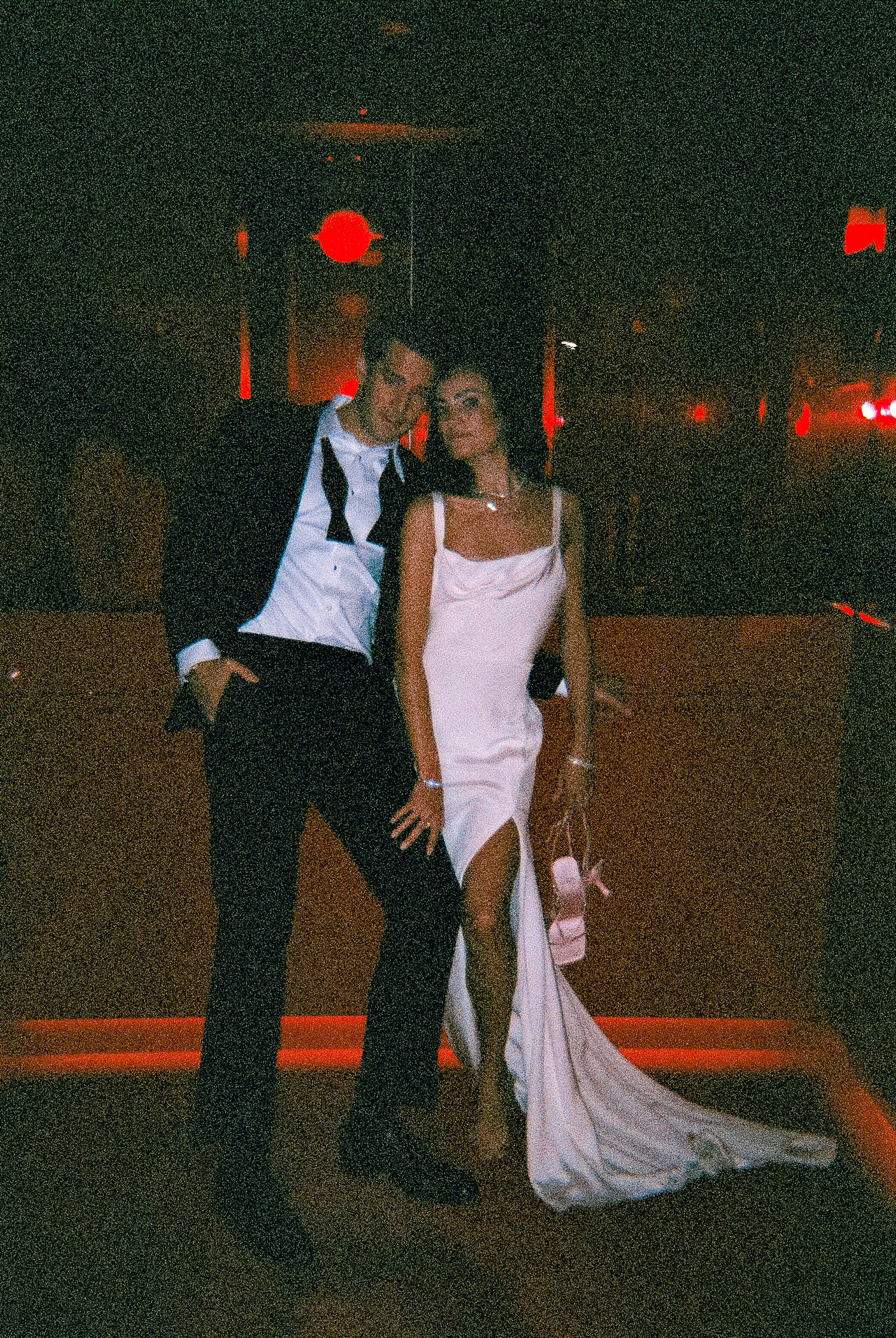 Man in black tuxedo leaning on woman in white dress red elevator Virgin Hotel Dallas