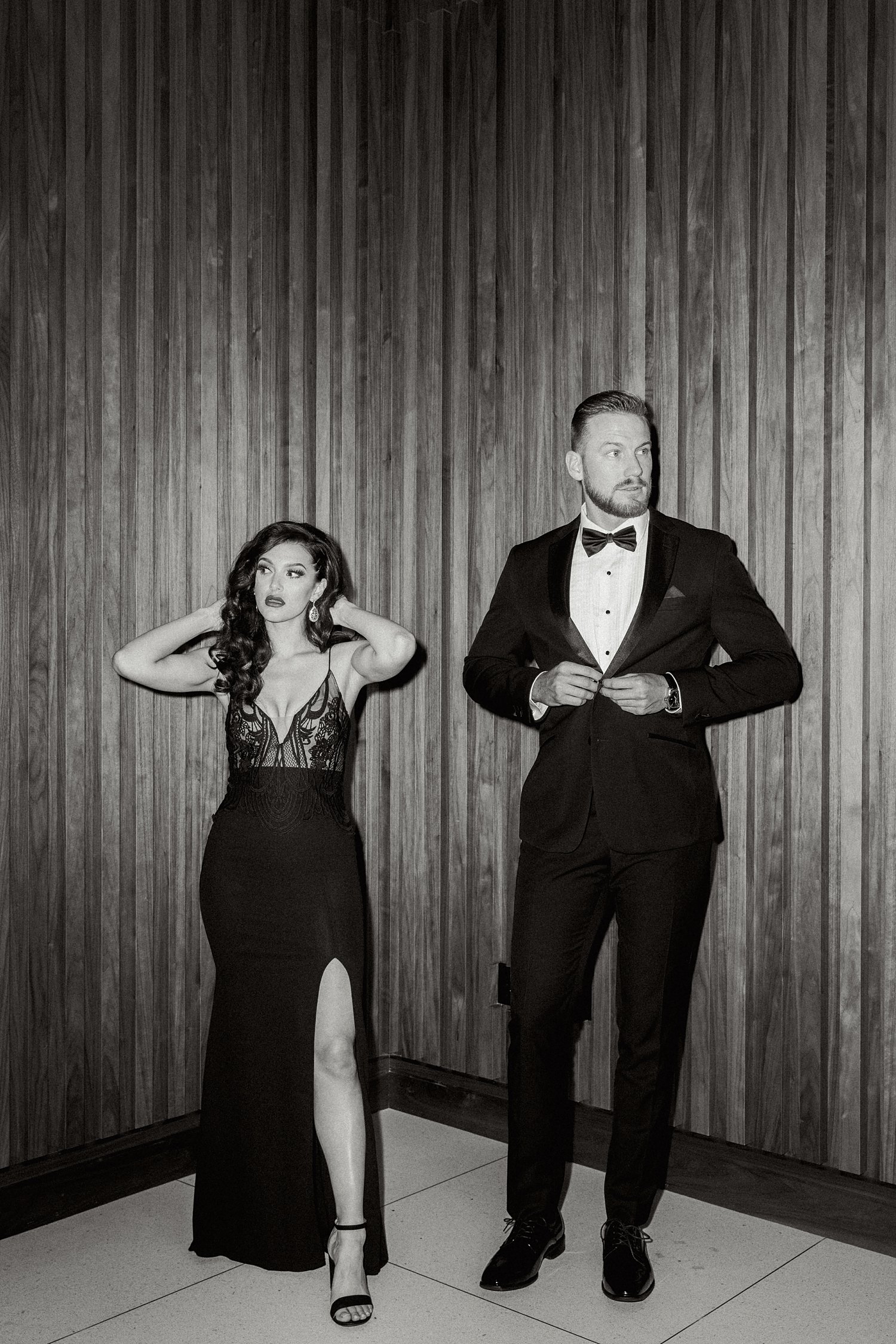 Woman in black dress and man in tuxedo standing in front of wood paneled wall