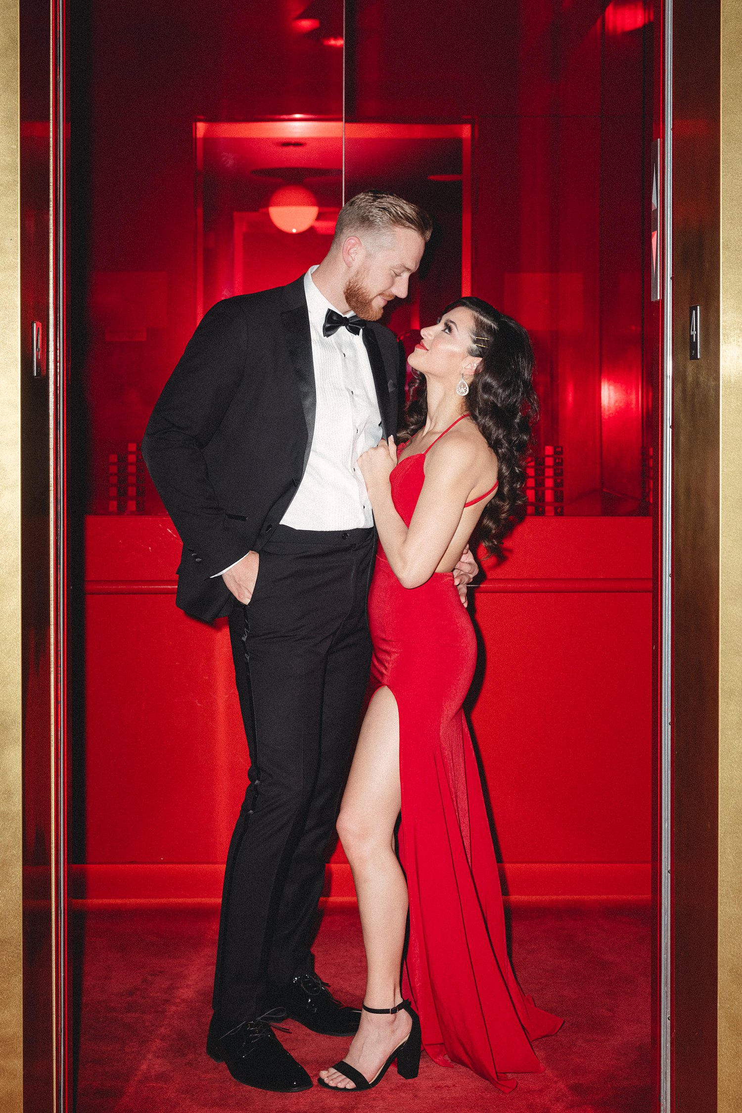 Woman in Red Dress and man in black tuxedo standing together in Virgin Hotel elevator Dallas Engagement