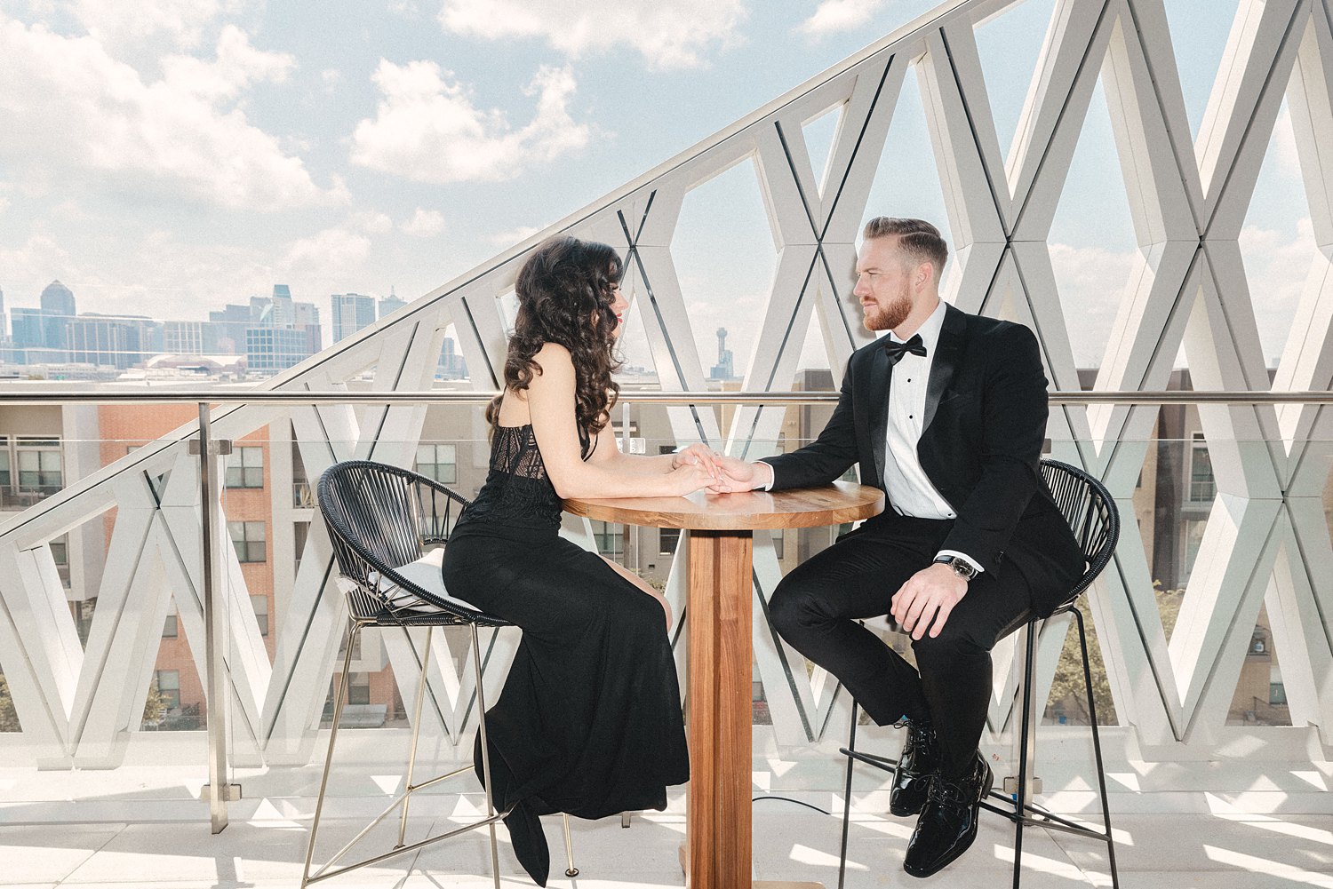 Woman in black dress and man in tuxedo sitting together at balcony table Virgin Hotel Dallas