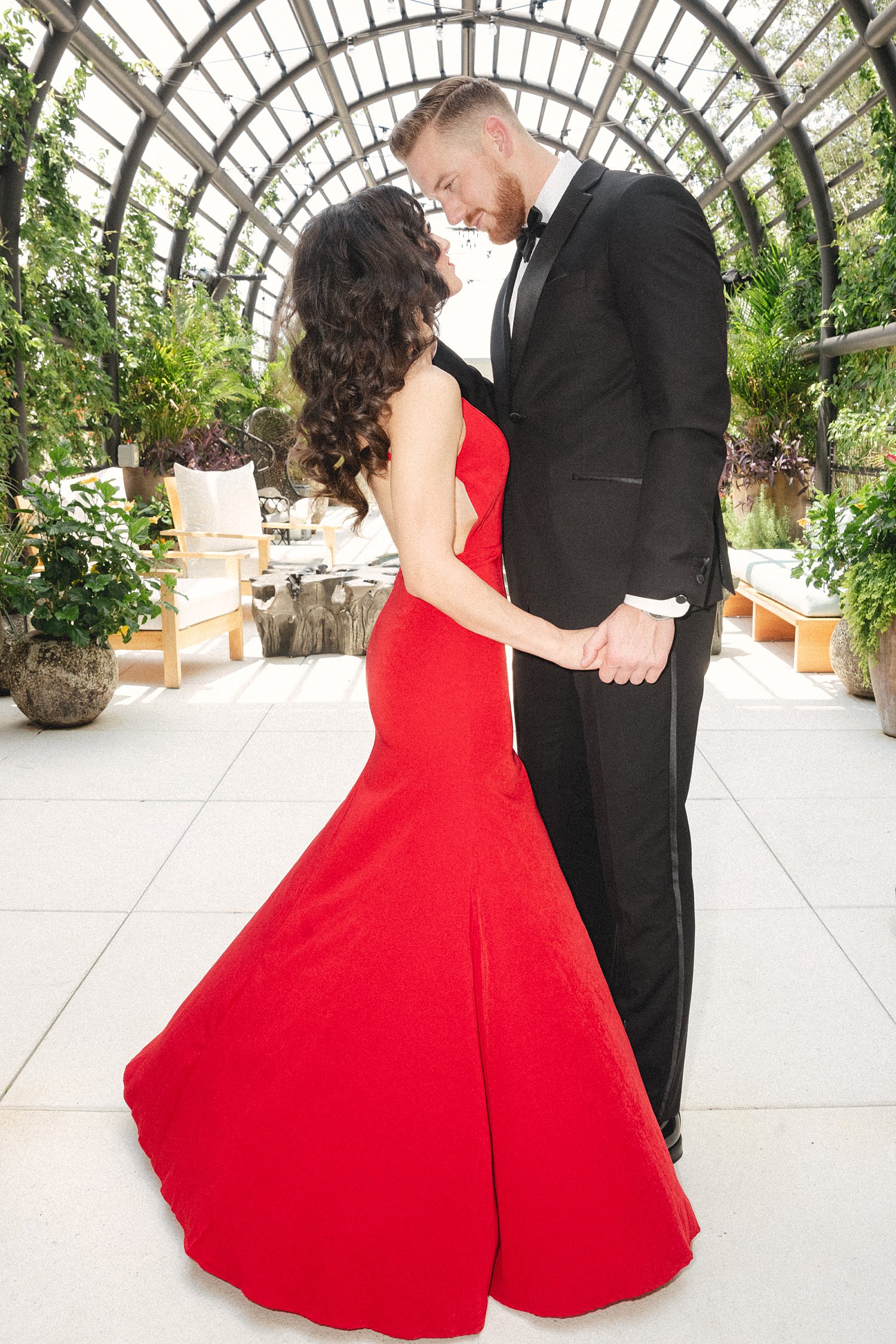 Woman in red Dress standing with man in black tuxedo by outdoor garden