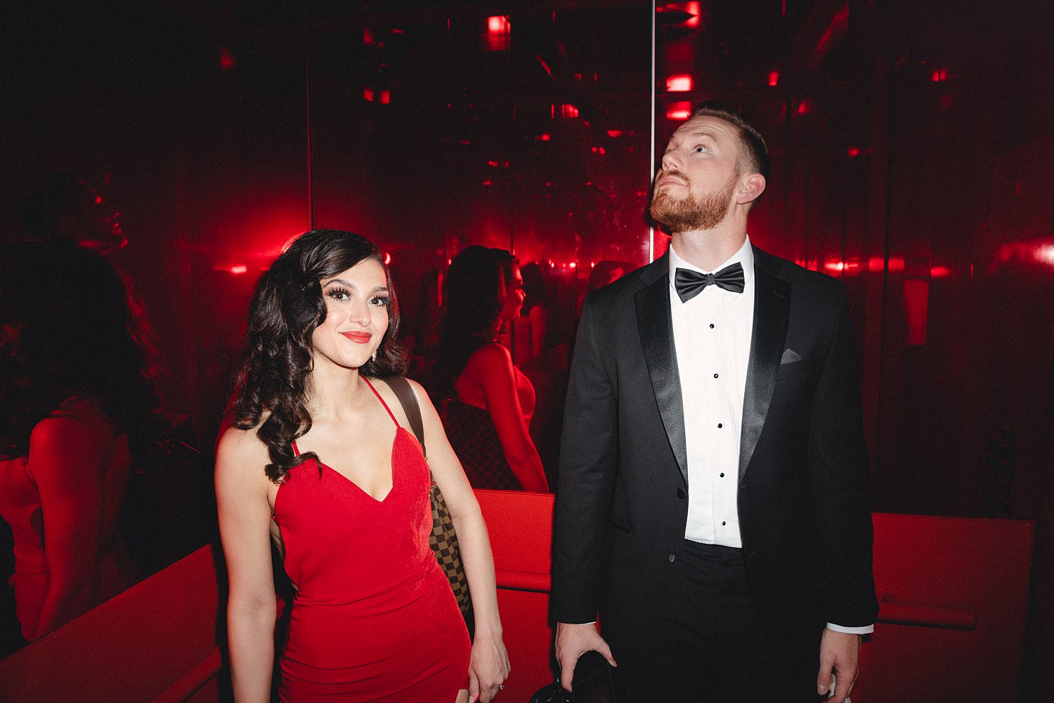 Woman in Red Dress and man in black tuxedo standing together in Virgin Hotel elevator