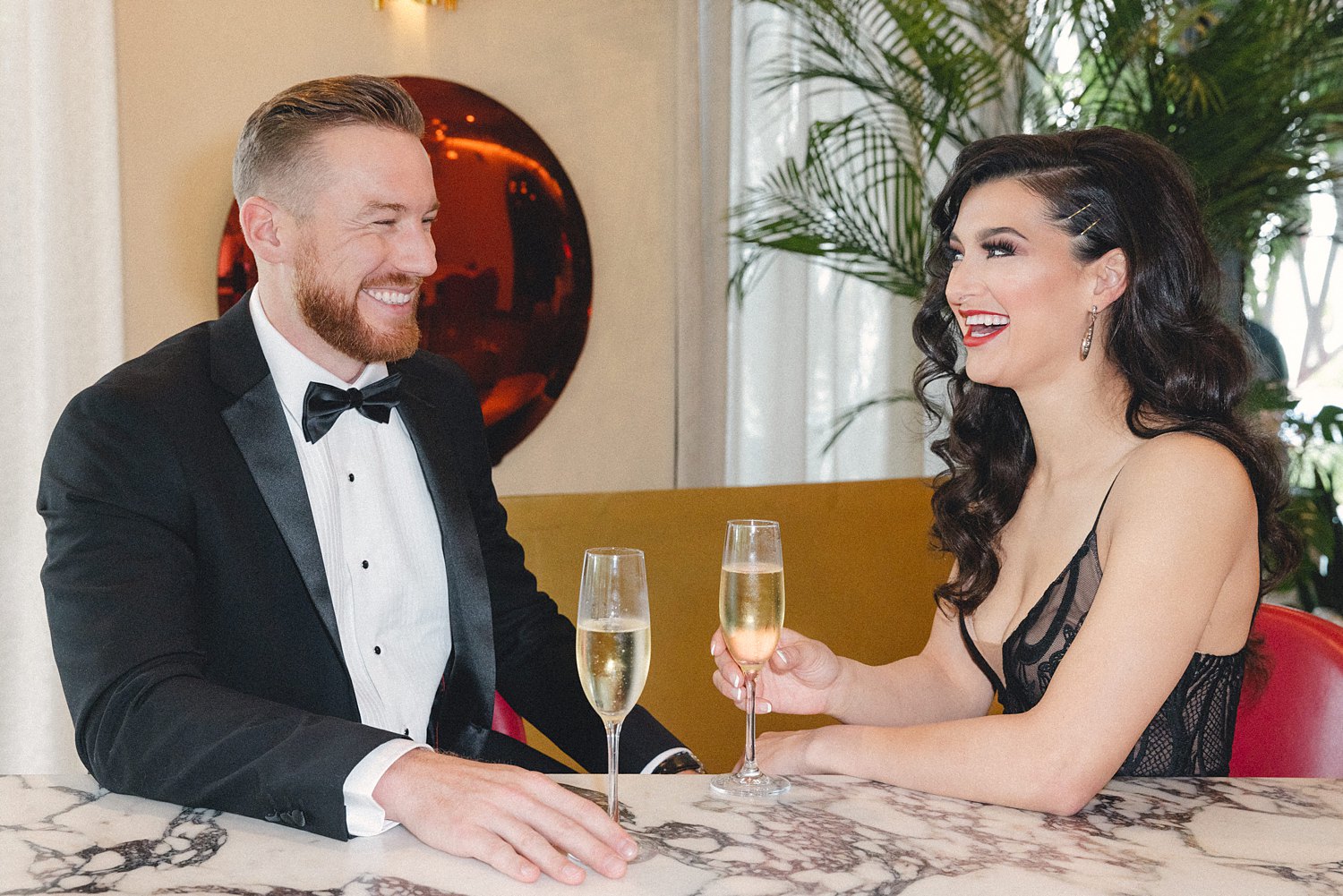 Woman in black dress and man in tuxedo drinking at bar at Virgin Hotel Dallas