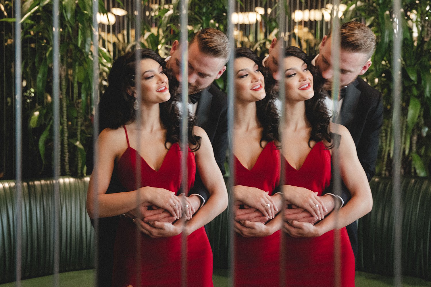Woman in red Dress being hugged by man in black tuxedo reflected in mirrored lounge wall