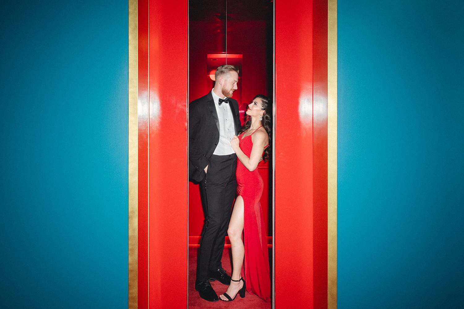 Woman in Dress and man in black tuxedo standing together in Virgin Hotel red elevator Engagement