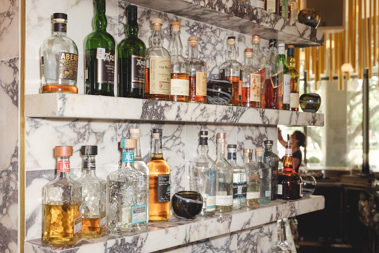 liquor bottles on white marble shelves at Dallas Virgin Hotel Bar