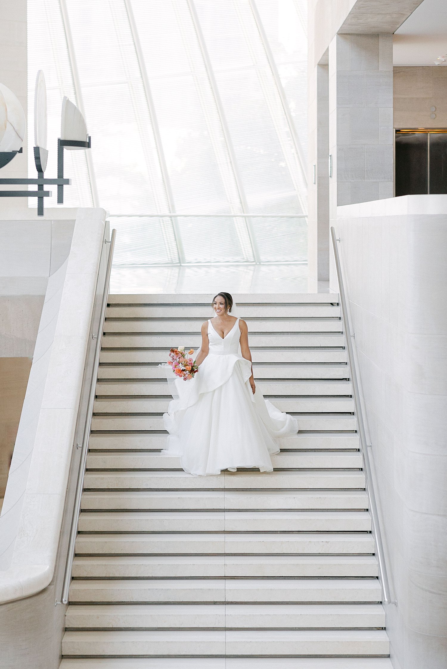 Bride in white wedding dress holding bouquet and walking down stair case Dallas Arts District