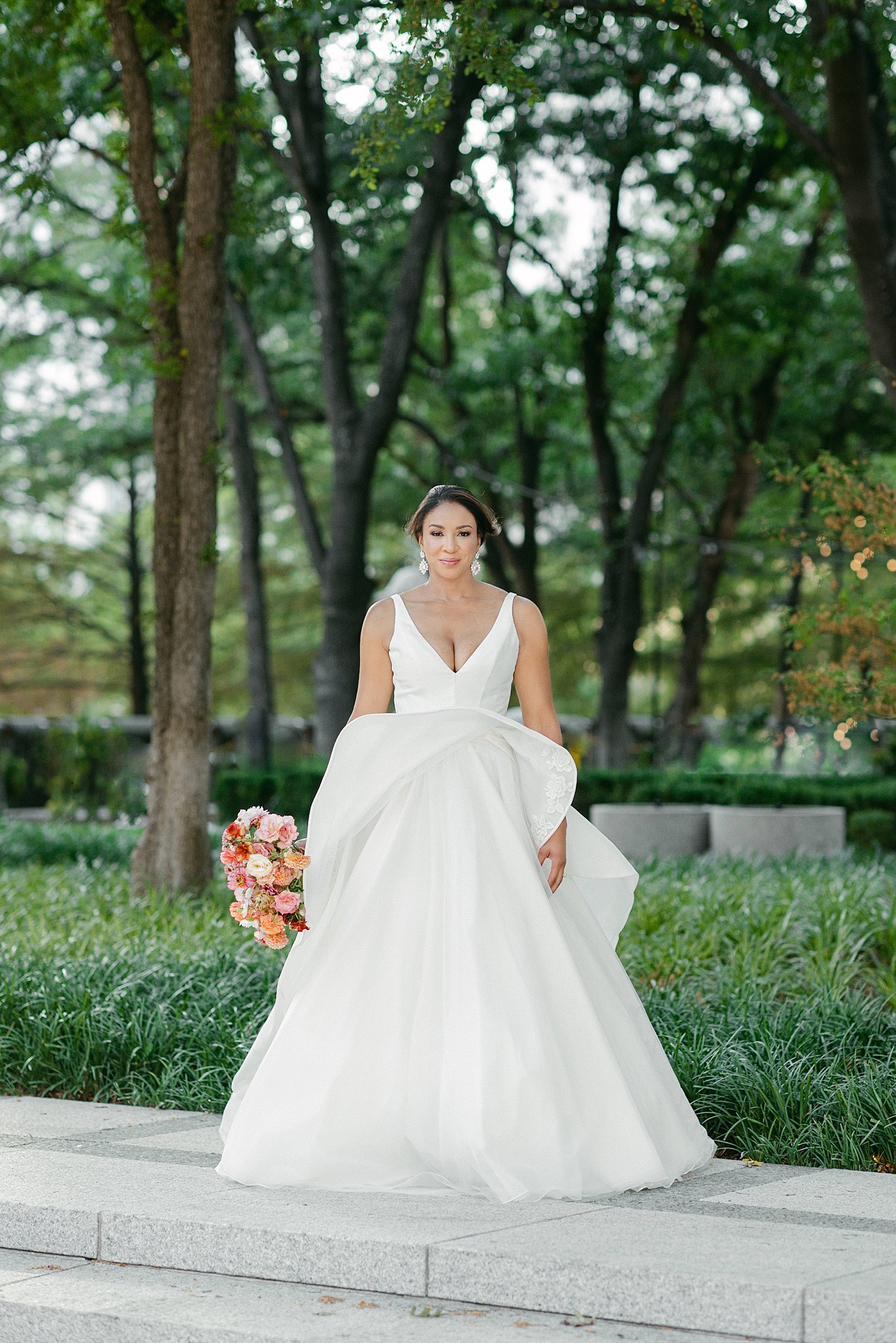 Bride in white wedding dress holding colorful floral bouquet outside in green garden