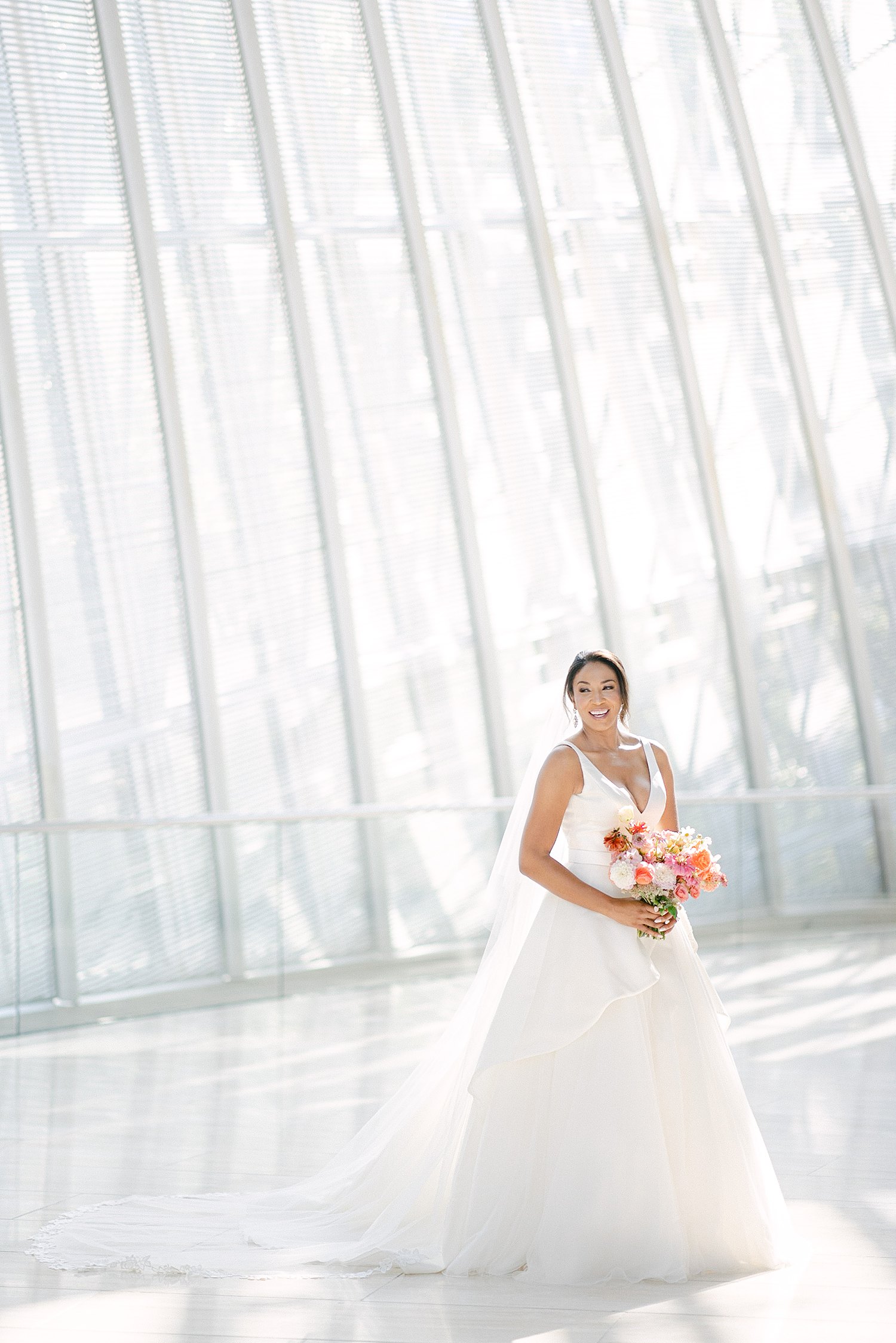 Bride in white wedding dress holding colorful floral bouquet smiling Dallas Arts District