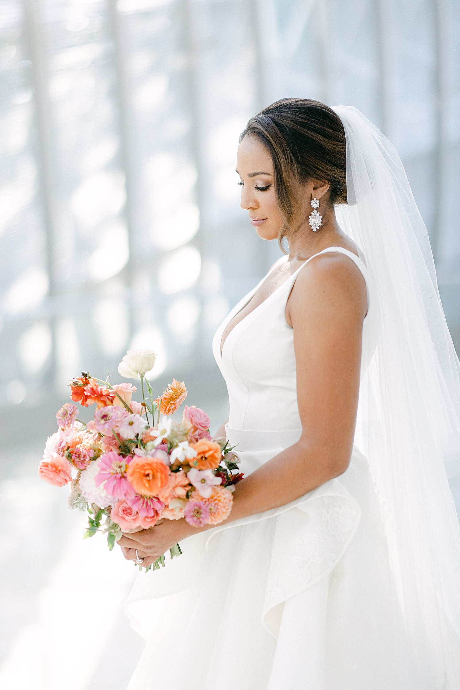 Bride in white wedding dress looking at colorful floral bouquet