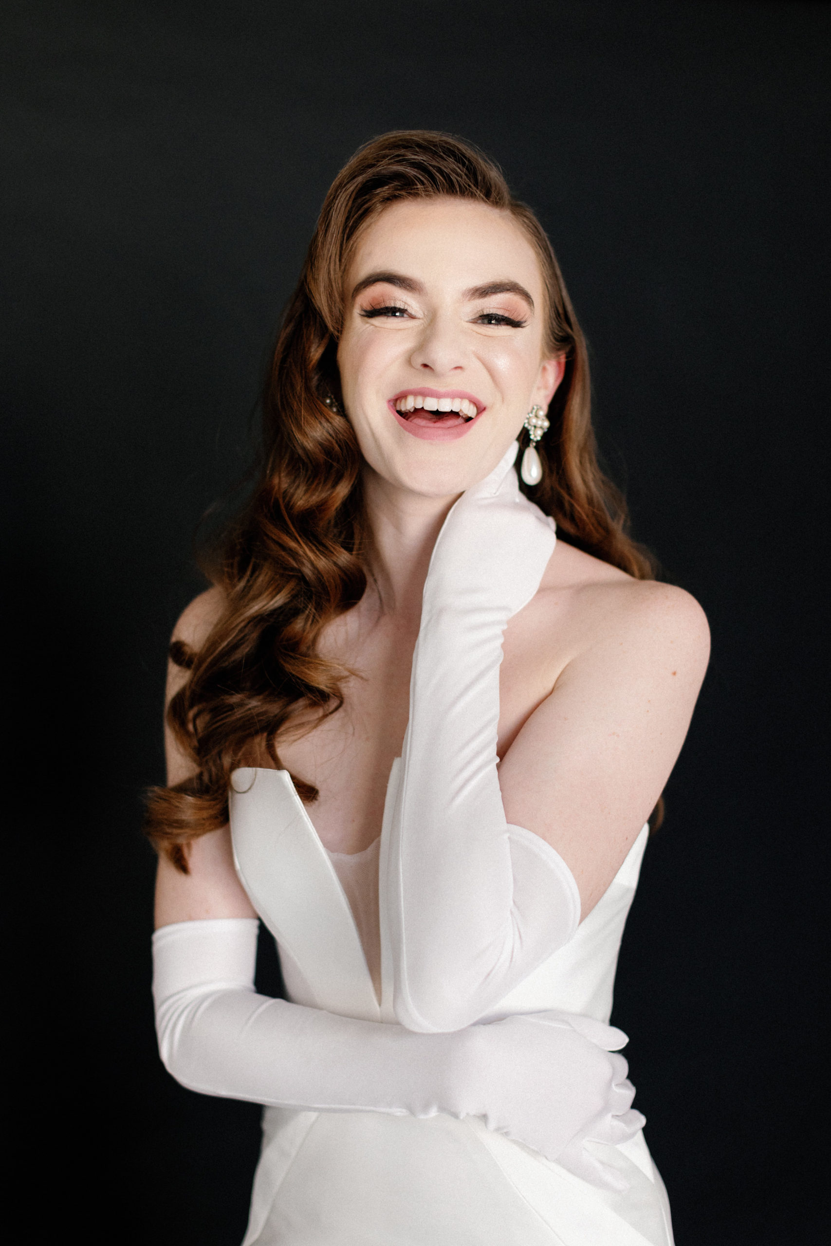 Bride in white dress and gloves laughing against black backdrop