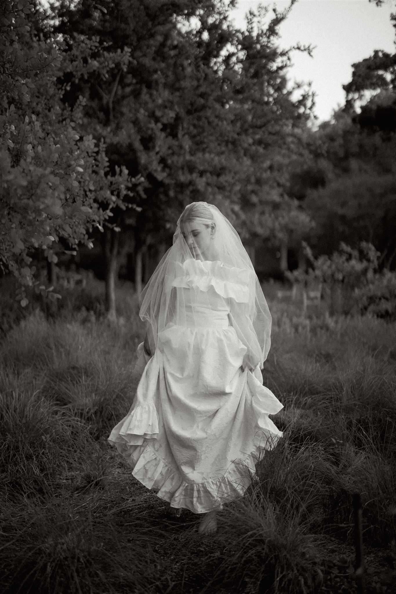 Bride in white wedding dress and veil walking in grass