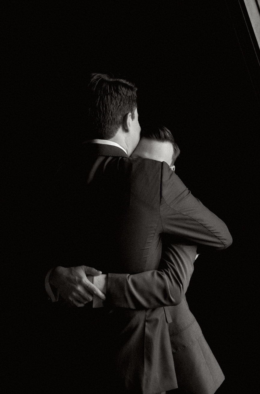 Two men hugging against black background