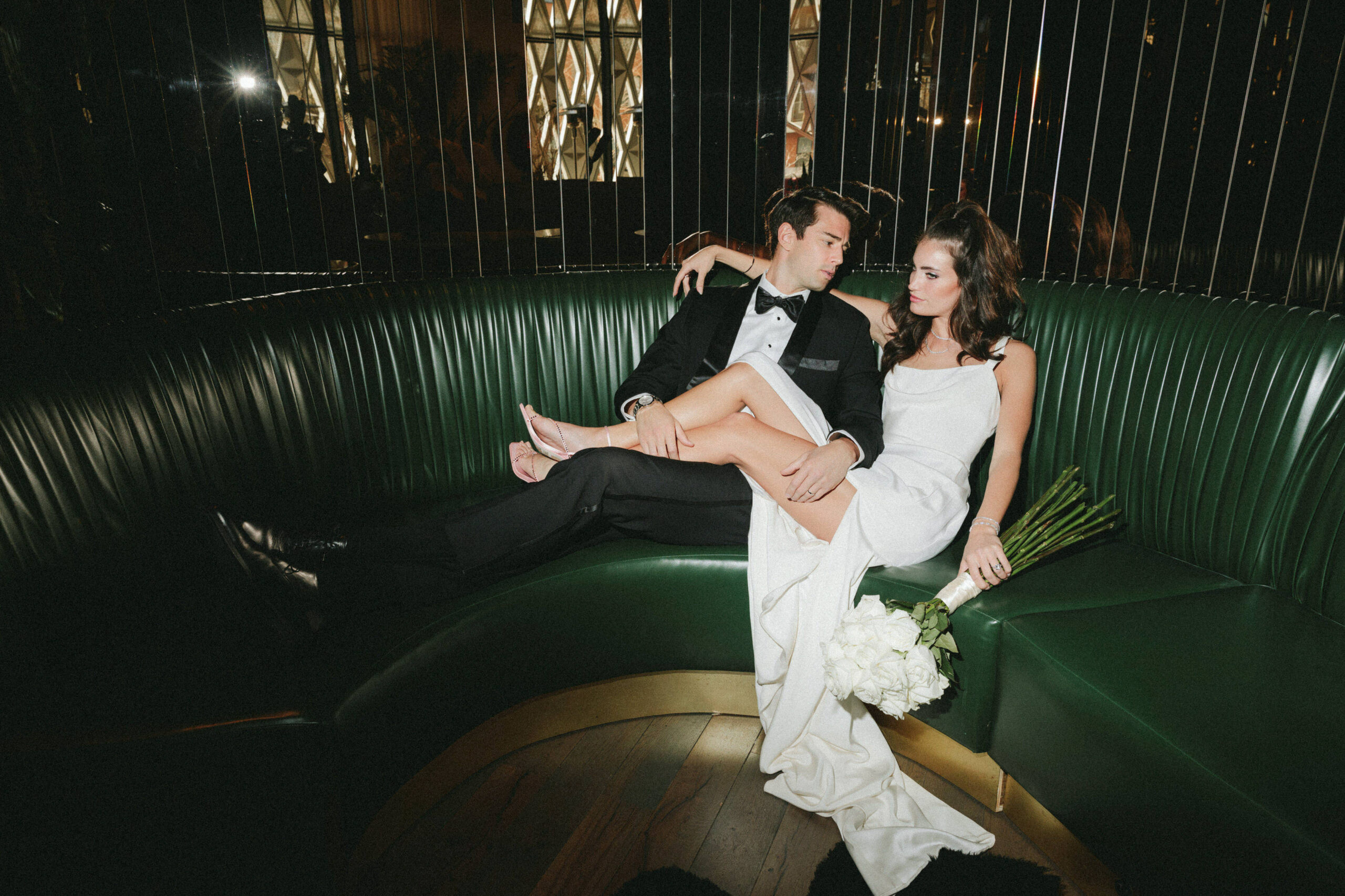 bride sitting next to groom on green couch in wedding dress.
