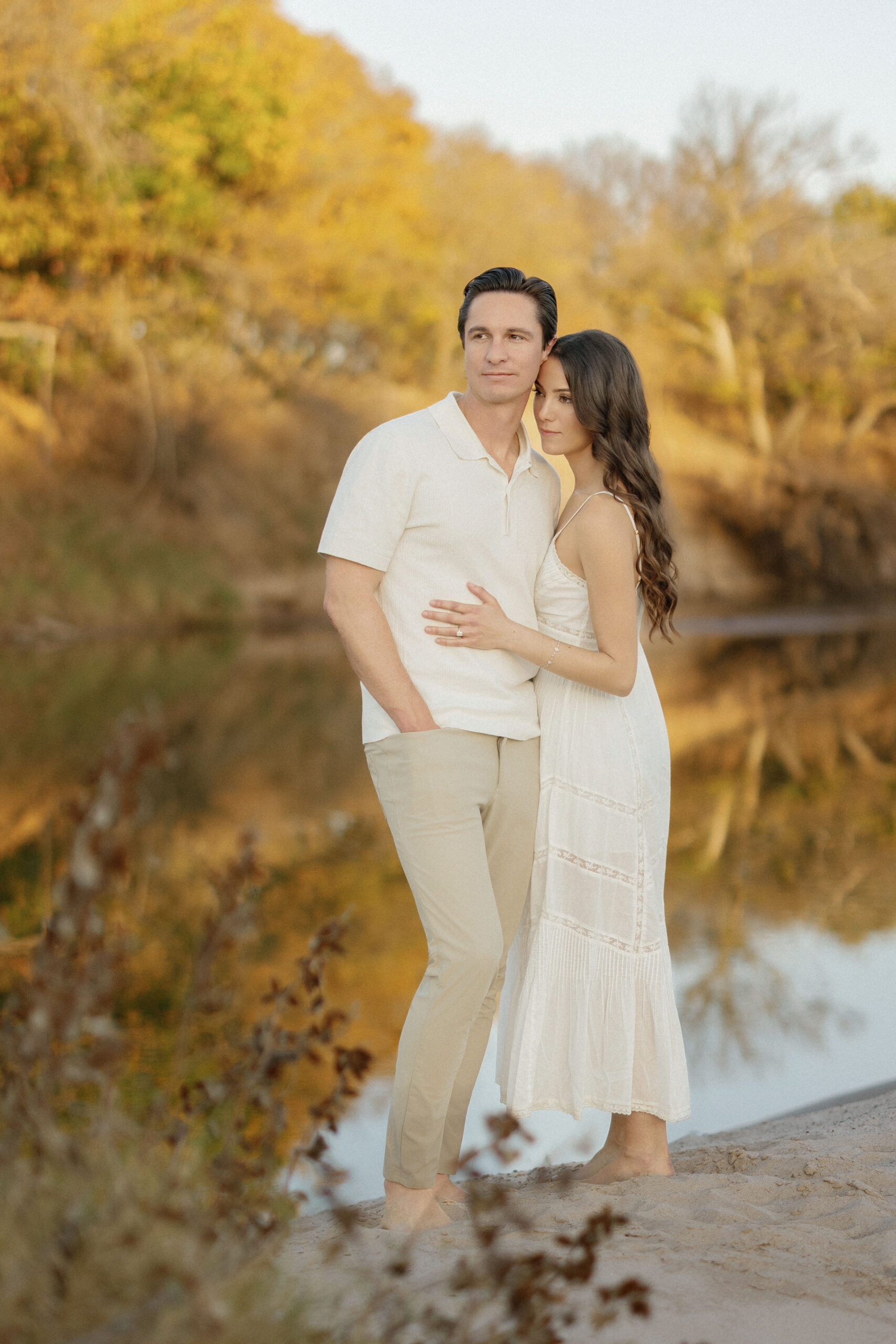 Fiancé and bride-to-be embracing along the Brazos River sand during sunset.